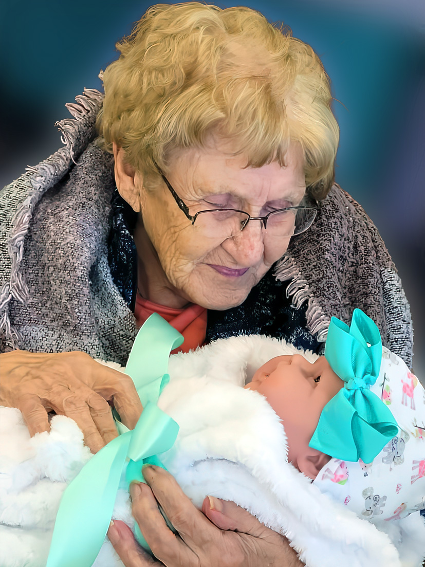 Elderly woman holding a Pearl's Memory Baby therapeutic doll during memory care activity